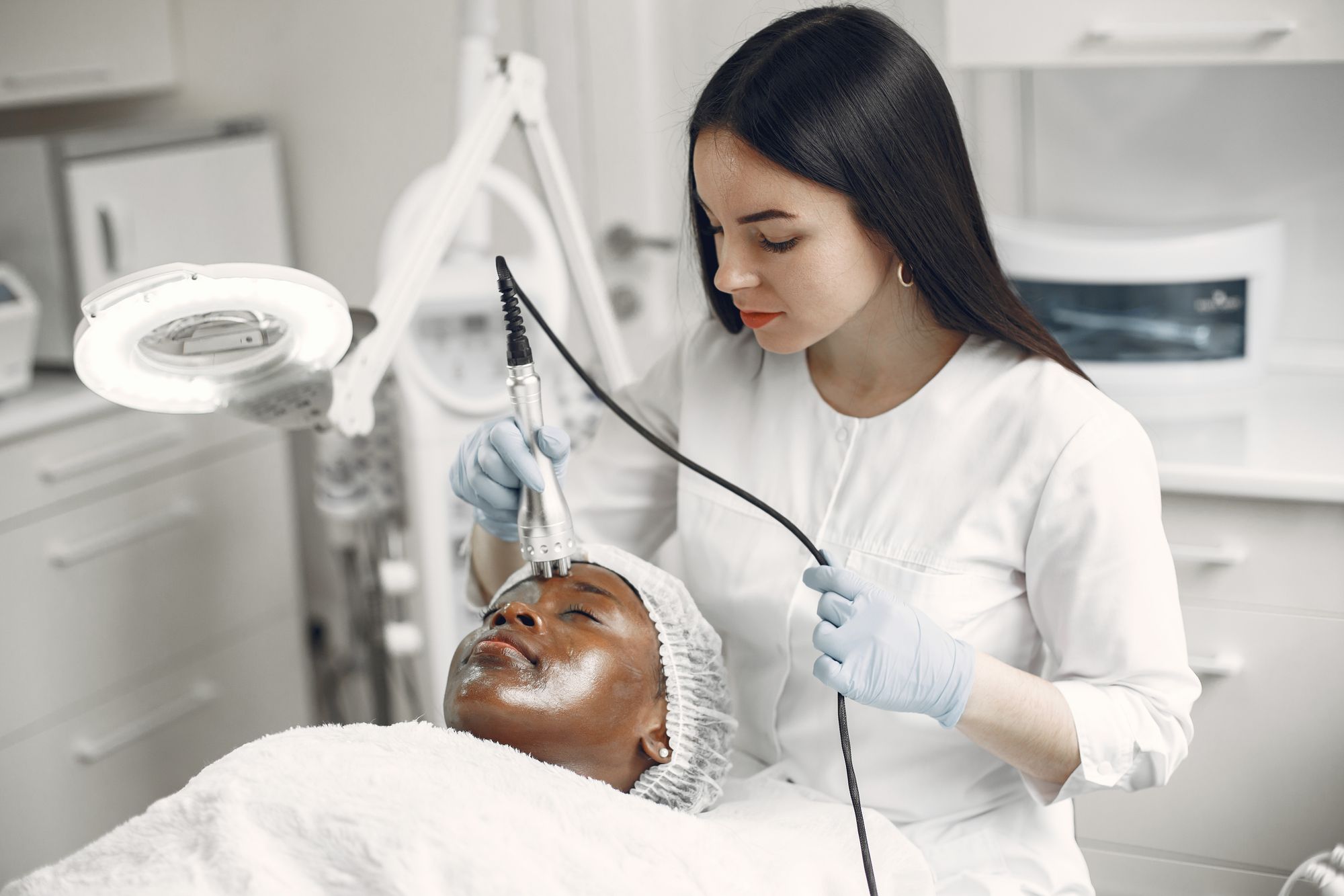 Clinician using a non-graphic aesthetic skin device in a neutral white treatment room.