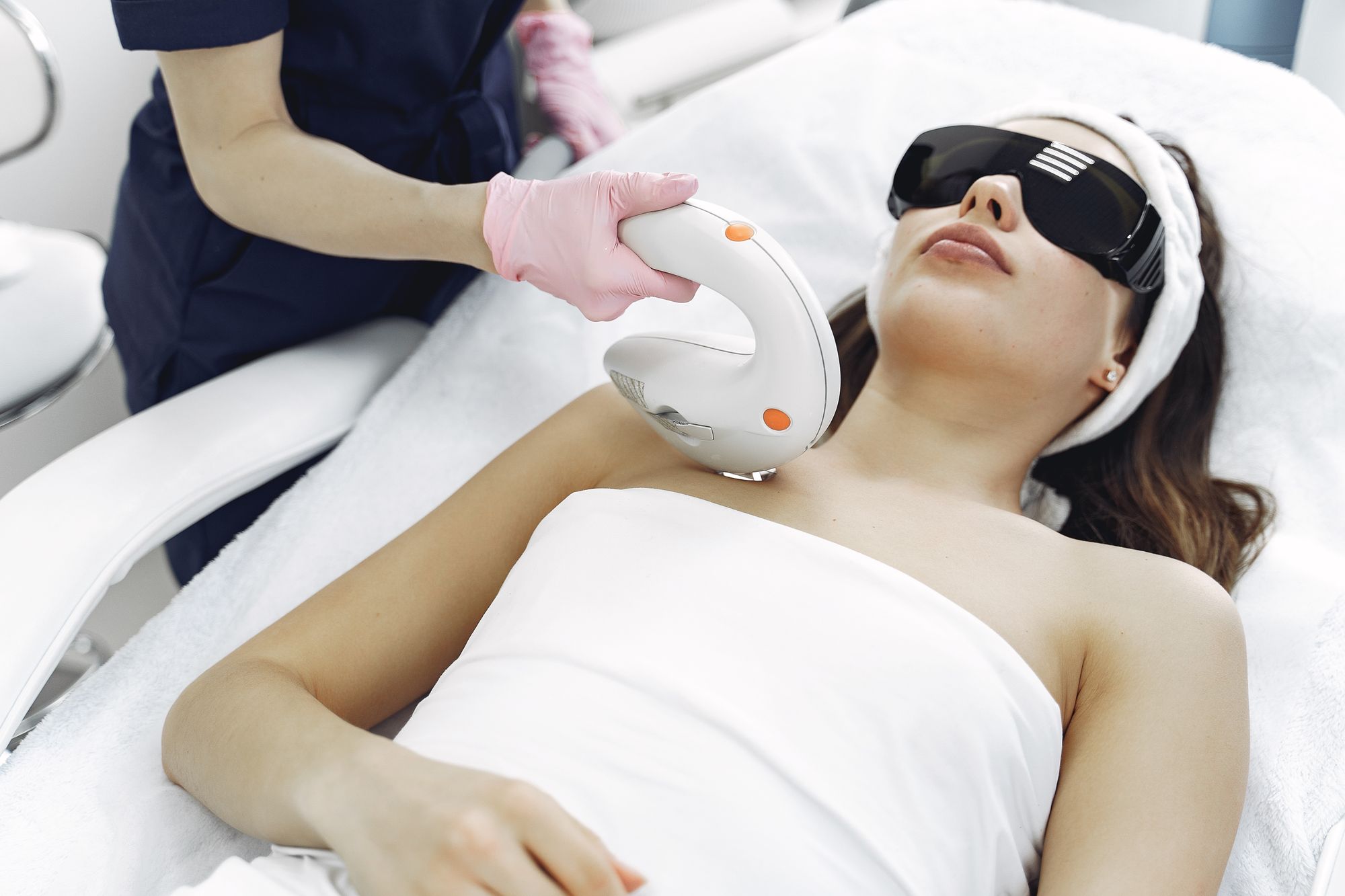 Recognizable light/laser aesthetic treatment device and client in protective glasses.