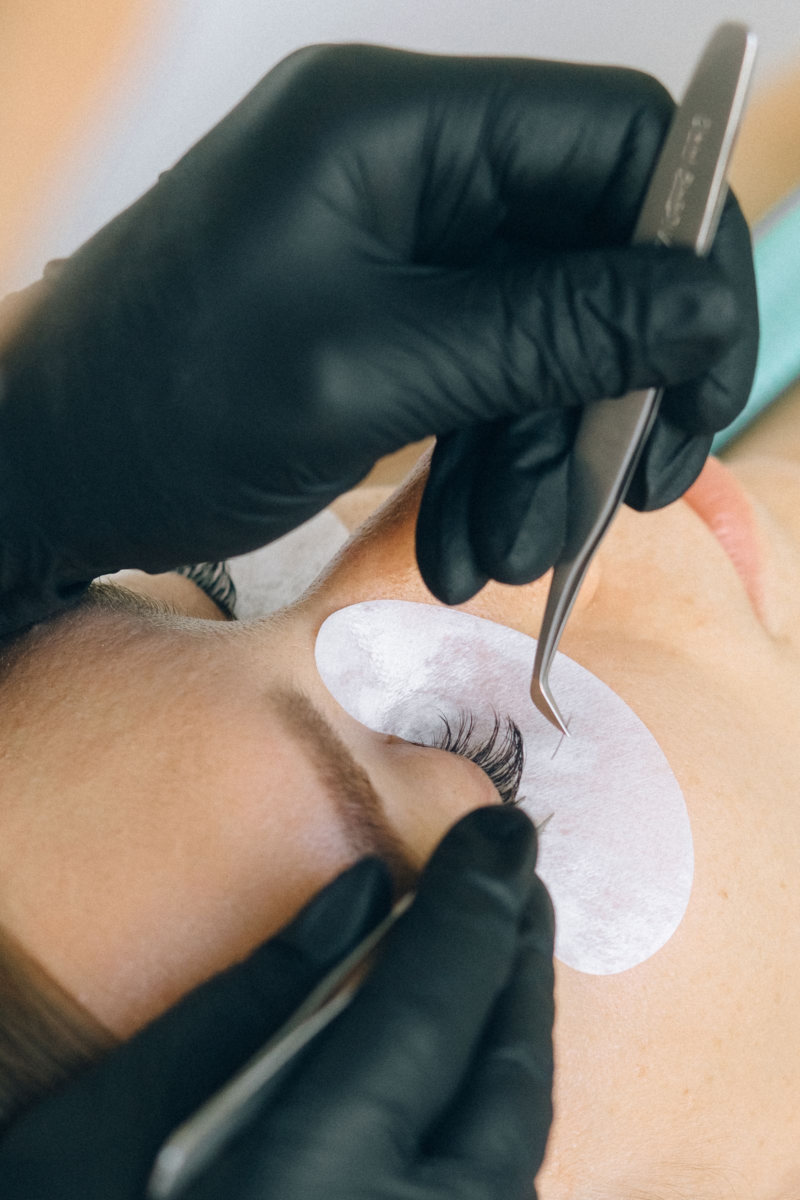 Technician applying eyelash extensions with tweezers and protective under-eye pads